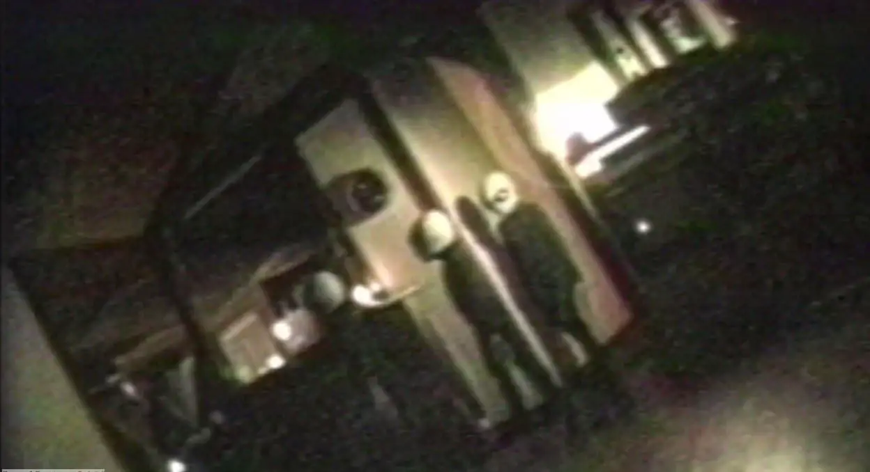 a tilted screen shot from a video camera of three small alien creatures walking into the living room of a house