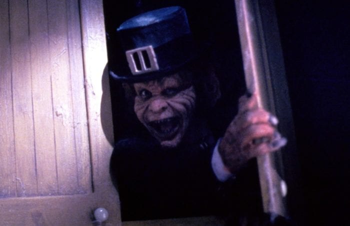 A leprechaun grimaces as he looks out from a wooden cabinet.e
