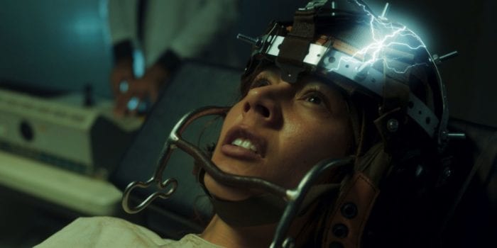 Alma (Martina Garcia) has a helmet device wrapped about her head, emitting electrical currents.