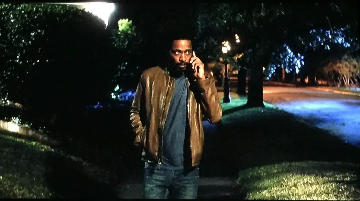 Man walks down the sidewalk on a dark street while talking on the phone.