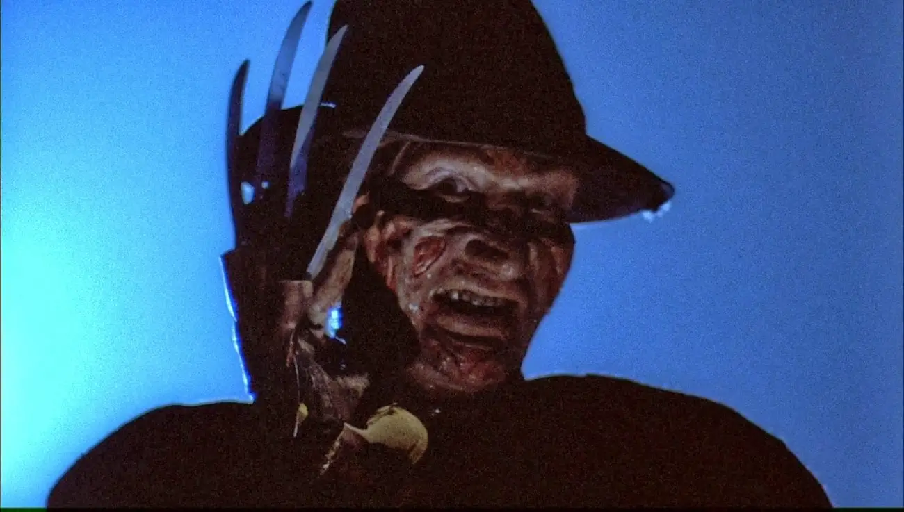 Freddy Krueger raises his blade fingers to his face.