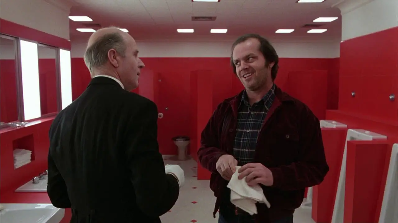 Jack Torrance and Delbert Grady stand talking in a red bathroom in The Shining.