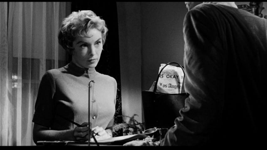 Janet Leigh as Marion Crane looks up at Norman Bates with pen poised to sign hotel guest book.
