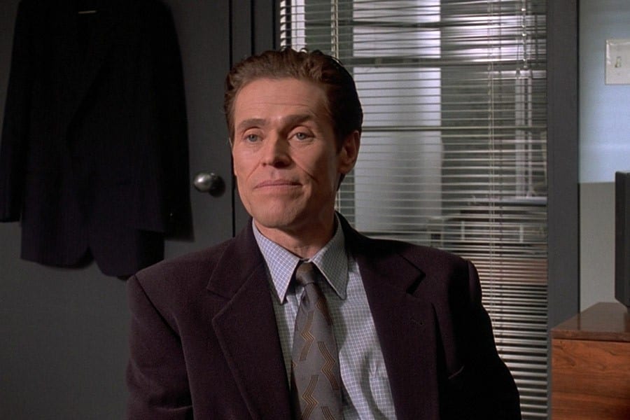 Willem Dafoe as detective sits in an office in American Psycho.