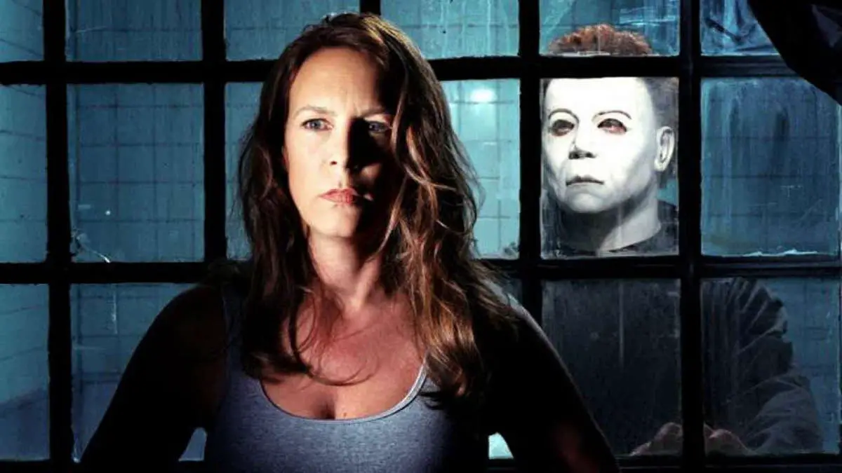 Laurie Strode stands in front of a window with Michael Myers standing behind her.