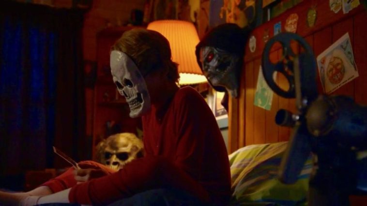 Boy in skeleton mask sits on bed
