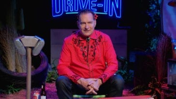 Joe Bob sitting in front of The Last Drive-In sign