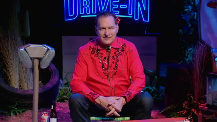 Joe Bob sitting in front of The Last Drive-In sign