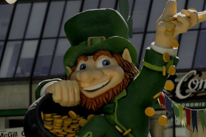 A smiling leprechaun waves as he holds his legendary pot of gold.a
