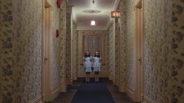 Two blonde girls stand holding hands at the end of a hallway in The Shining.