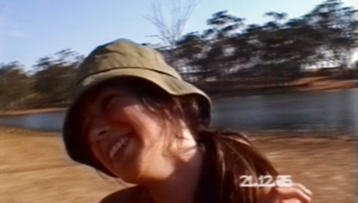 A screenshot of a home video showing a young girl in a hat smiling happily.