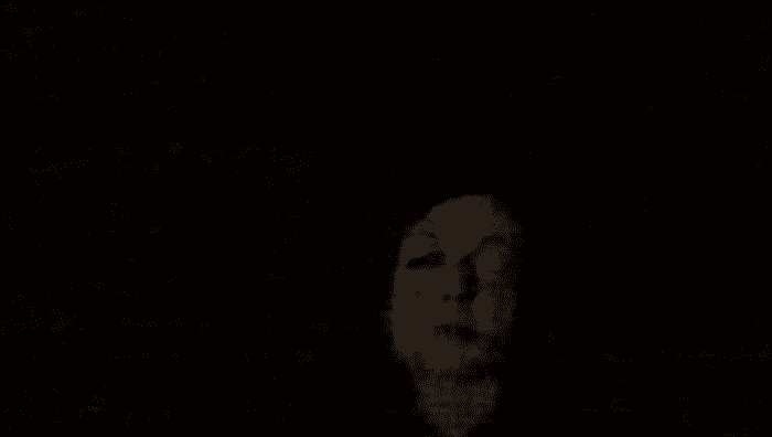 A disfigured white face appears amongst a black background.