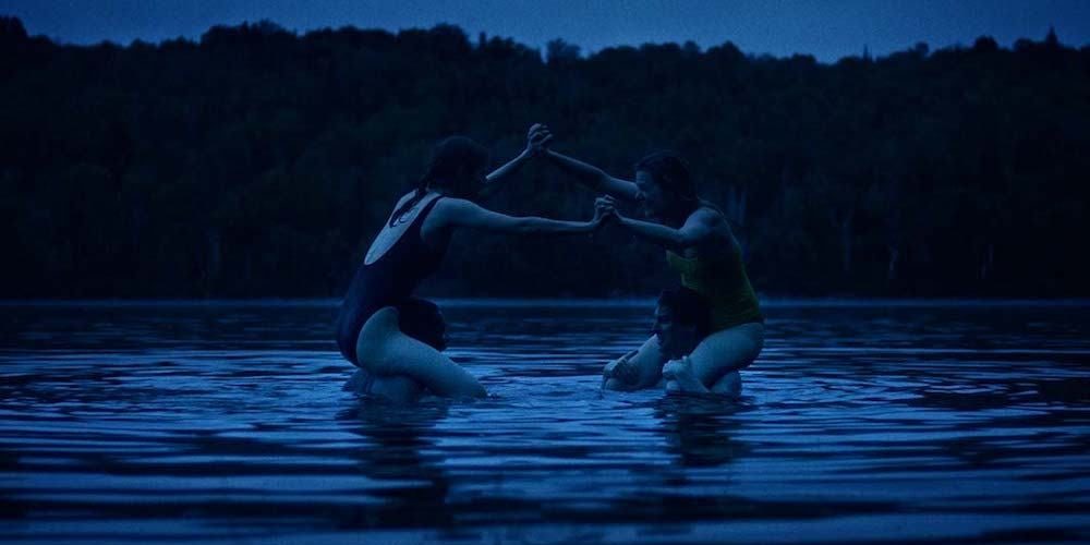 Two women sitting on two men's shoulders playfully fight in a lake in Violation
