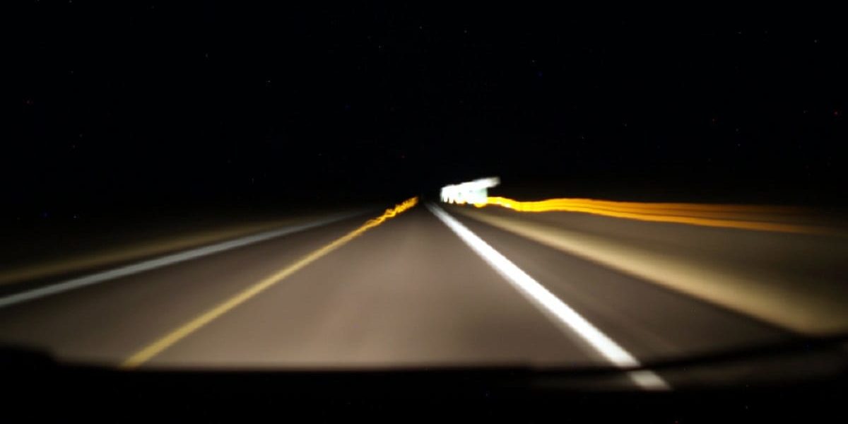 Blurred image of headlights shining on an extremely dark highway.