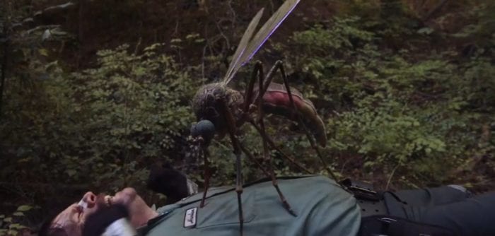 A gigantic mosquito sucks blood from Harlan's chest while on the ground with a pained look on his face