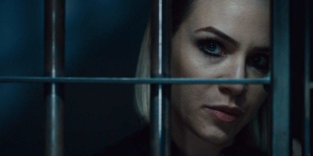 A blonde woman looks through the bars of a jail cell in Vicious Fun