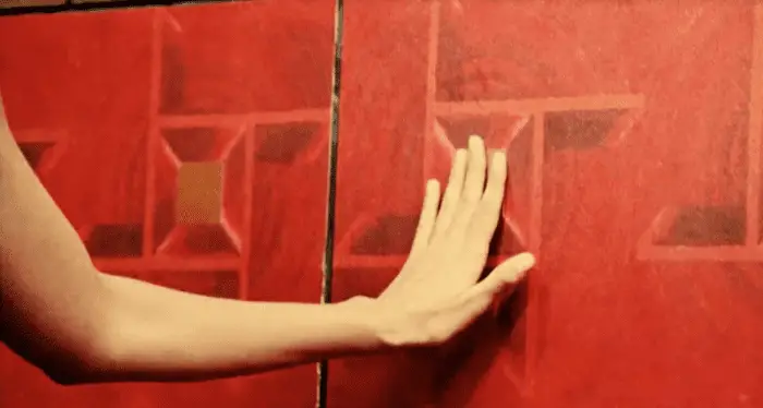 Oliva's hand touching the pattern in the red wallpaper
