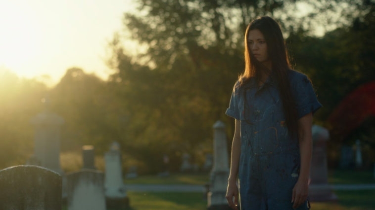 A woman in a blue dress in a graveyard at sunset in She Watches from the Woods