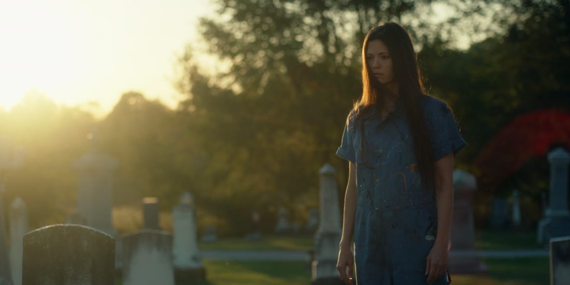 A woman in a blue dress in a graveyard at sunset in She Watches from the Woods
