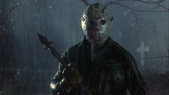 Jason Voorhees is standing in the rain and holding a weapon.