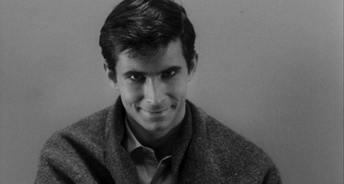 Close-up of a sinister young man wrapped in a blanket smiling into the camera.