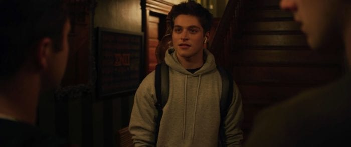 A young man wearing a hoodie and headphones looks at two other boys facing him in the foreground of the image.