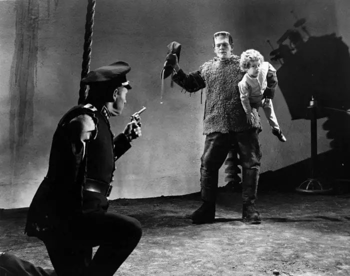 Frankenstein holding a child in front of a police officer