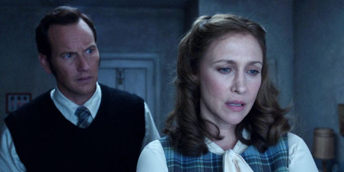 In the foreground to the right, a Lorraine Warren wearing a plaid dress, a kerchief tied around her neck, a contemplative look on her face; slightly behind her to the left, from the chest up Ed Warren, looks on in concern.