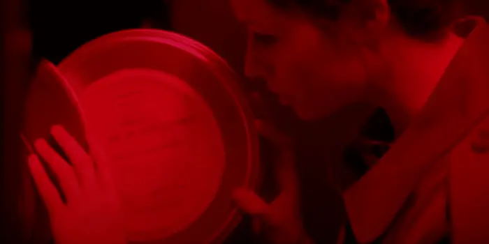 Enid examines a film reel in a red lit room in Censor