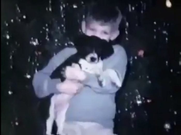 A little boy hugs a black and white puppy.