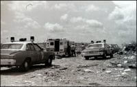 Two police cars and an ambulance search a landfill for a corpse