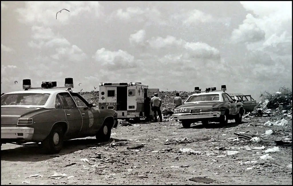 Two police cars and an ambulance search a landfill for a corpse