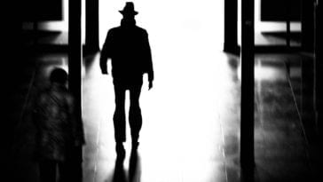 A shadow figure of a man walks down a dark hallway.