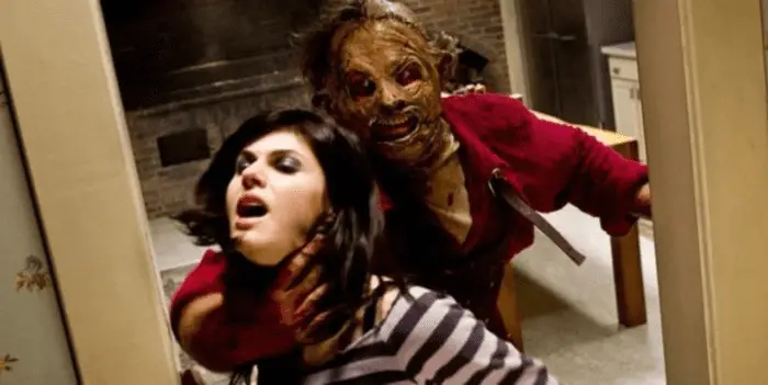 Alexandra Daddario as Heather Miller; behind her is Leatherface in stitched up skin mask, his hand grasped around her throat.