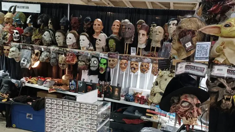A booth at decorated with many creepy masks, trinkets, figures, and a smaller display of colored contacts. There is a QR code to the right that says "scan me".