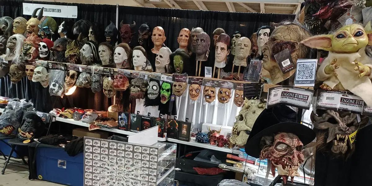 A booth at decorated with many creepy masks, trinkets, figures, and a smaller display of colored contacts. There is a QR code to the right that says "scan me".