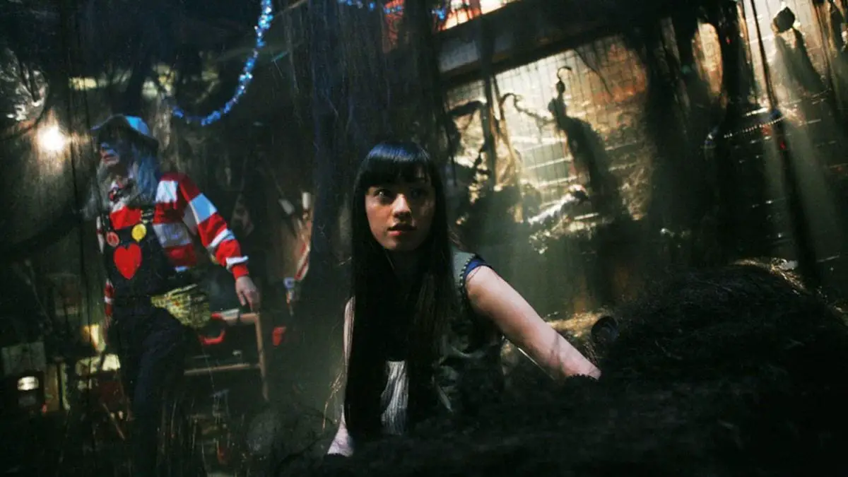 A young Japanese woman with long black hair, in a room filled with hair extensions. A man poses behind her.