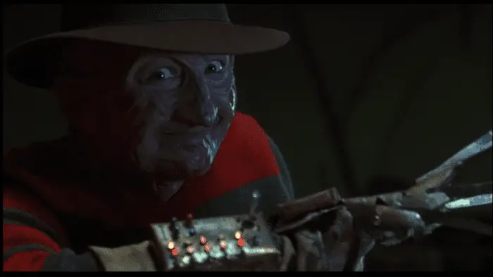 Robert Englund as Freddy Krueger in his trademark fedora, smiling and holding up his gloved hand, which has been transformed into a macabre Nintendo Power Glove.