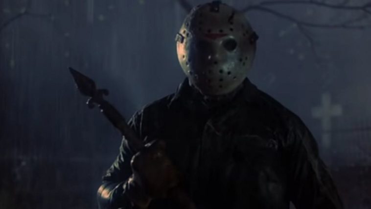 Jason Voorhees (C.J. Graham) standing in a cemetery at night in the rain. He is holding some sort of spear-type metal object.