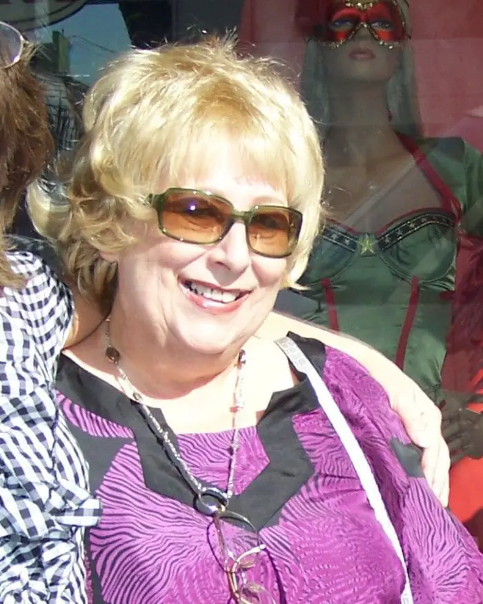 Sandra Niemi smiling for photograph, wearing sunglasses and a purple blouse.