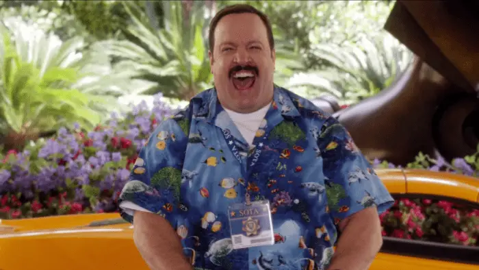 Kevin James as Paul Blart, wearing a fish-print short sleeve button-up and sporting a moustache; around his neck hangs his laminated mall cop "badge".