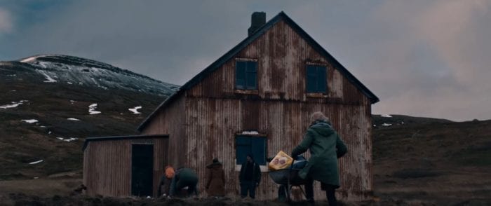 Several people carrying supplies and pushing wheelbarrows approach an old rusty house