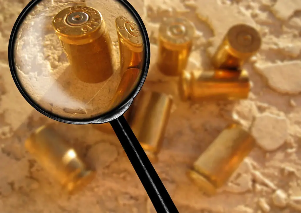 A magnifying glass analyses a set of bullets on the ground.