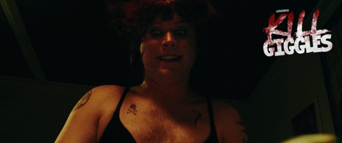 Tommy Dos Santos (Michael Ray Williams), a pale man with a hairy chest and various small tattoos dressed as a woman. He is wearing a black bra, a dark frizzy wig and dark makeup. He is looking down ward with a crazed look on his face.