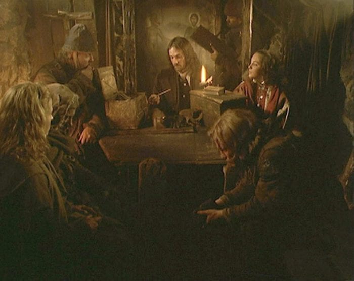 Several people crowd around a table drinking. The room is lit by candlelight