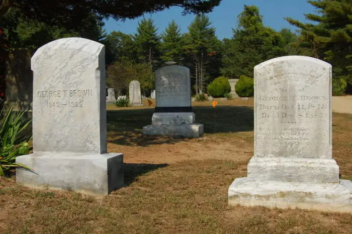 A day time shot of three grey stone headstones in a cemetery.