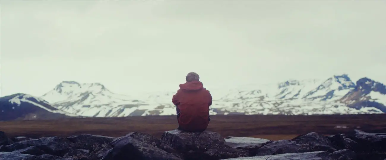 Einar sits alone on a hill in his red coat