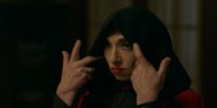 Naomi Grossman in American Horror Story: Apocalypse as Samantha Crowe, a white woman with red lips and dark eye makeup wearing a black hoot over her head. Her hands are raised to pull the hood back.