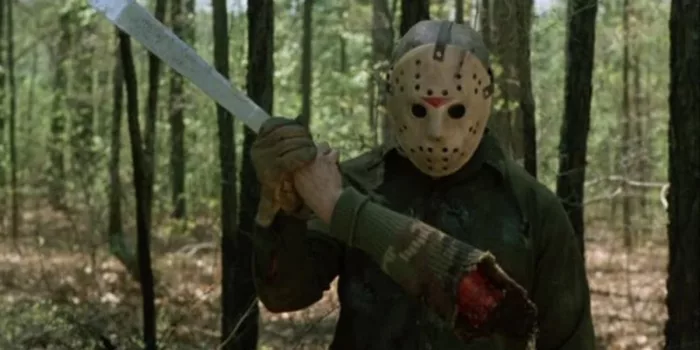 Jason holds up a severed arm after a kill, looking at it in complete curiosity.