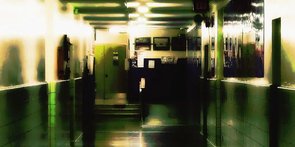 A badly lit, decrepit school hallway is barren of life